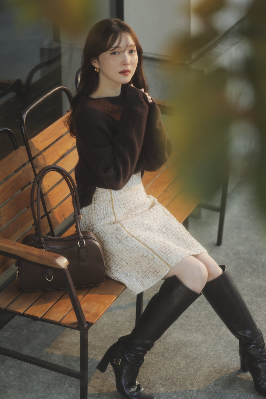 2WAYアンゴララクーン混ニット・ベロアラインツイードミニスカート・ロングブーツ・カーブラインボストンバッグ・ノットモチーフピアスを着用した女性