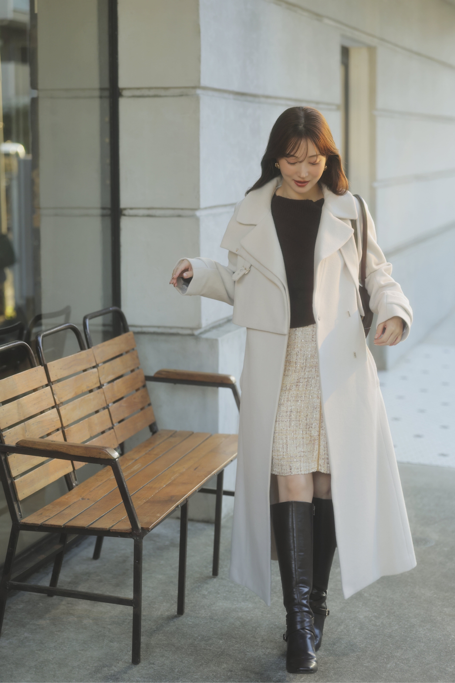 2WAYスタンドカラーウールコート・2WAYアンゴララクーン混ニット・ベロアラインツイードミニスカート・ロングブーツ・カーブラインボストンバッグ・ノットモチーフピアスを着用した女性