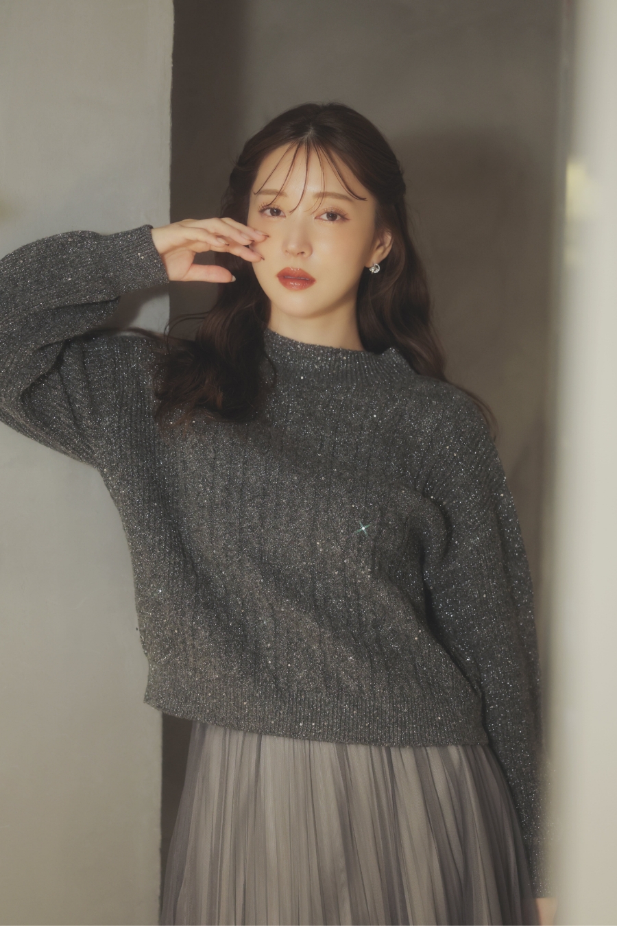 スパンコールラメケーブルニット・グラデイレヘムチュールスカート・ロングブーツ・トリプルビジューピアスを着用した女性