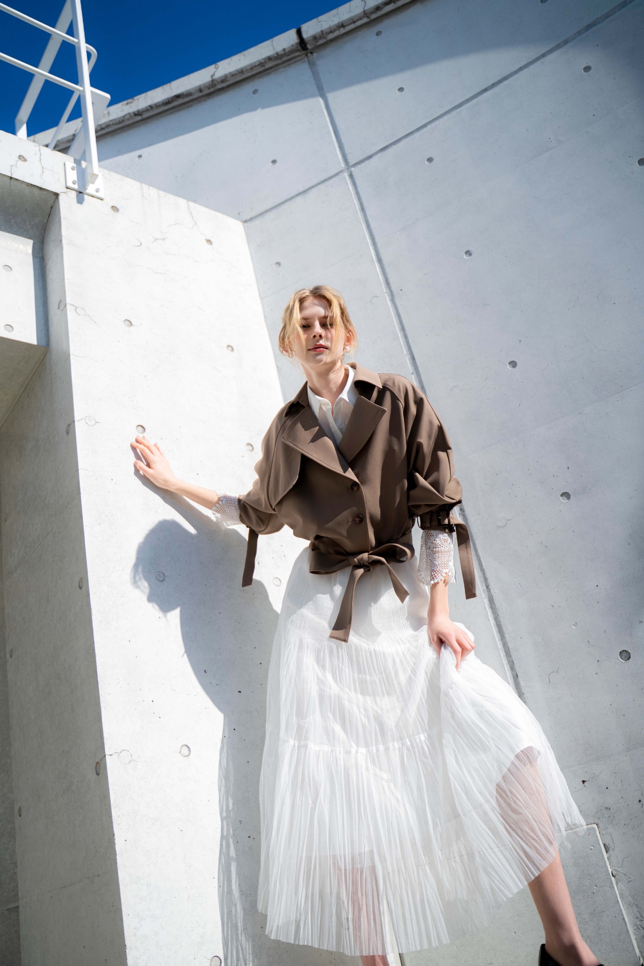 ラグランショートトレンチ・レースカフスシャツ・プリーツチュールスカート・スクエアビットローファーを着用した女性