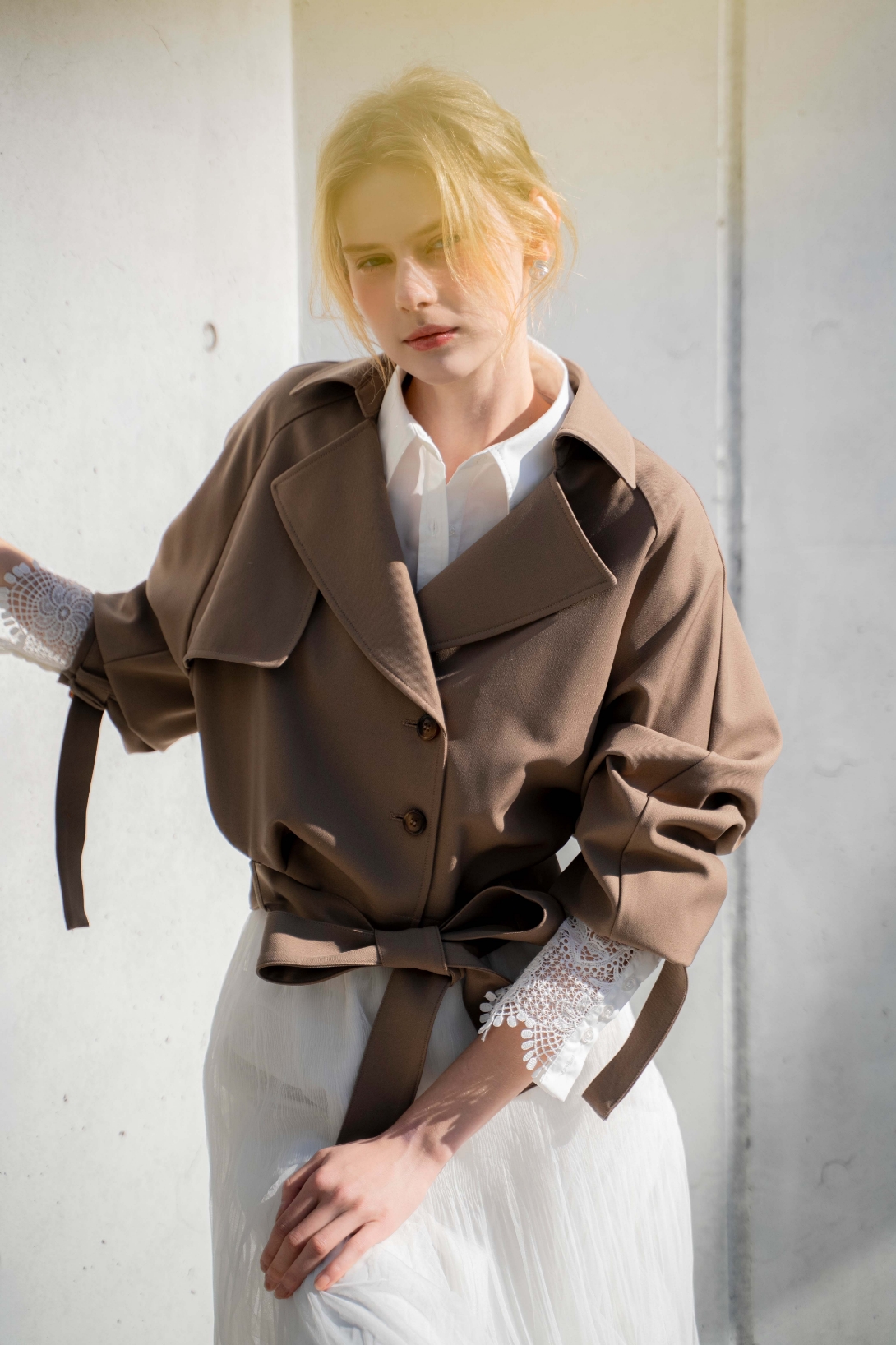 ラグランショートトレンチ・レースカフスシャツ・プリーツチュールスカートを着用した女性