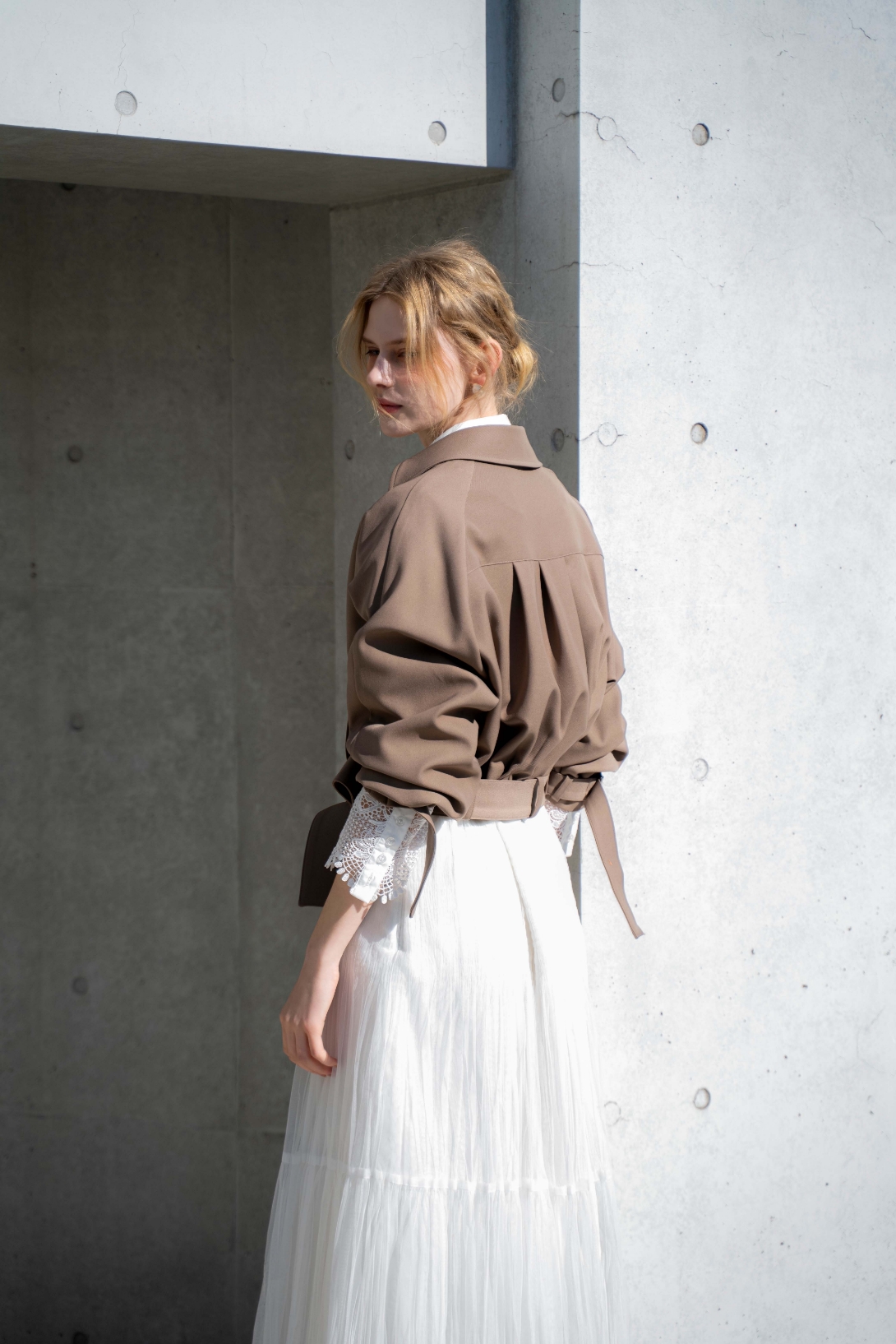 ラグランショートトレンチ・レースカフスシャツ・プリーツチュールスカートを着用した女性