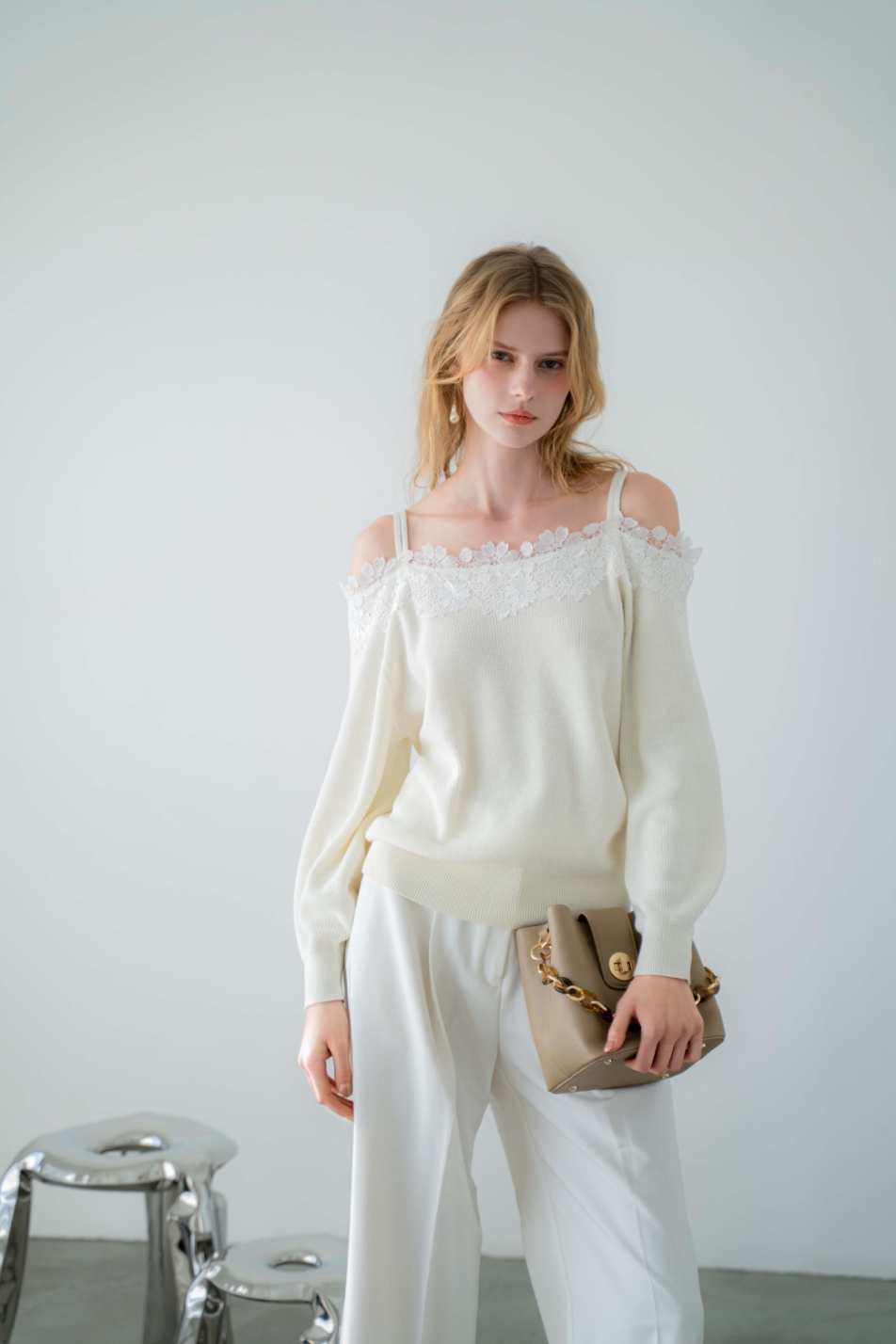 レーススリーブニット・ポケットデザインワイドパンツ・バックルデザインバケツバッグ・サイドノットパンプス・バロックパールアシメピアスを着用した女性