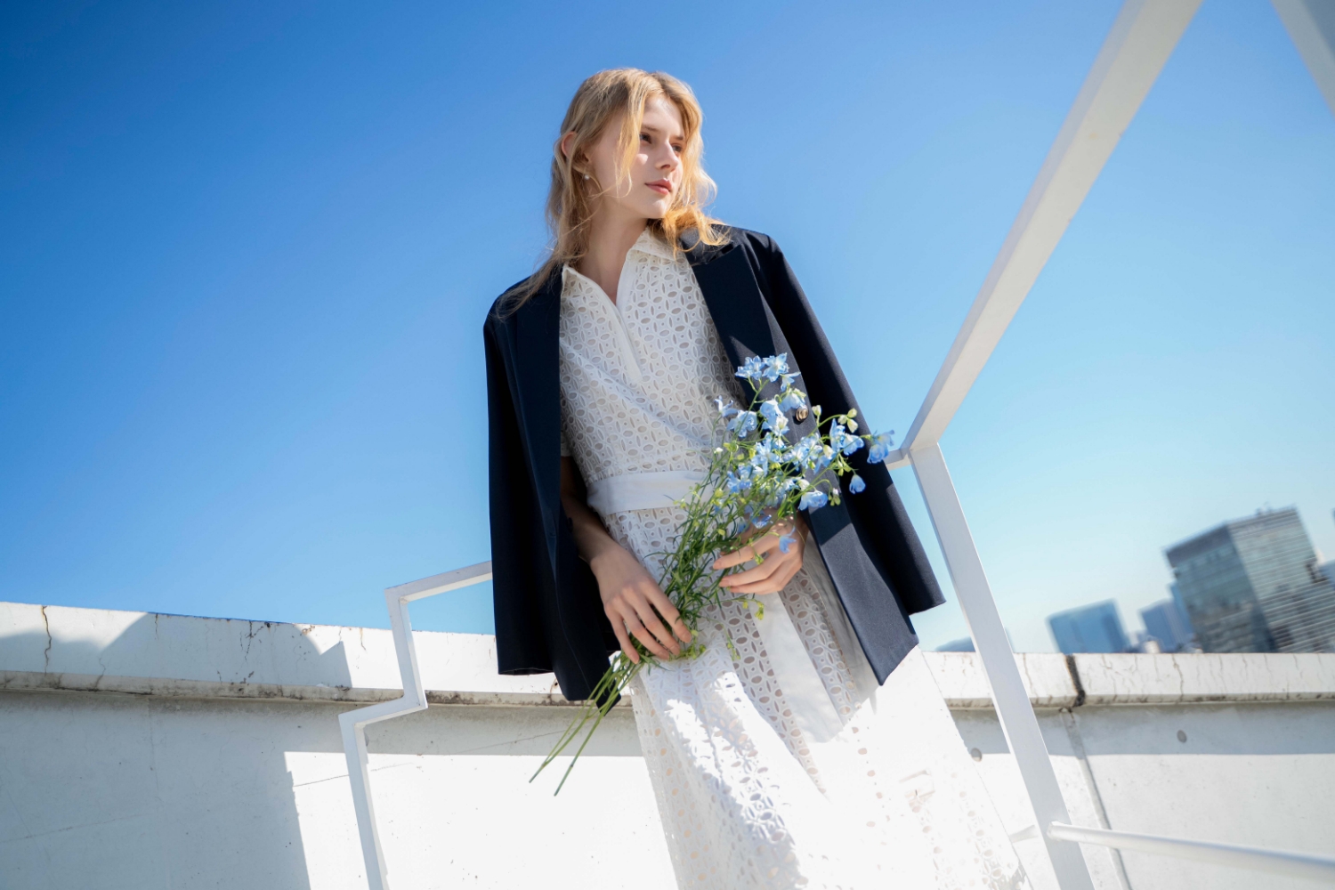 ダブルブレストジャケット・コットンレースシャツワンピース・スクエアビジューピアスを着用した女性