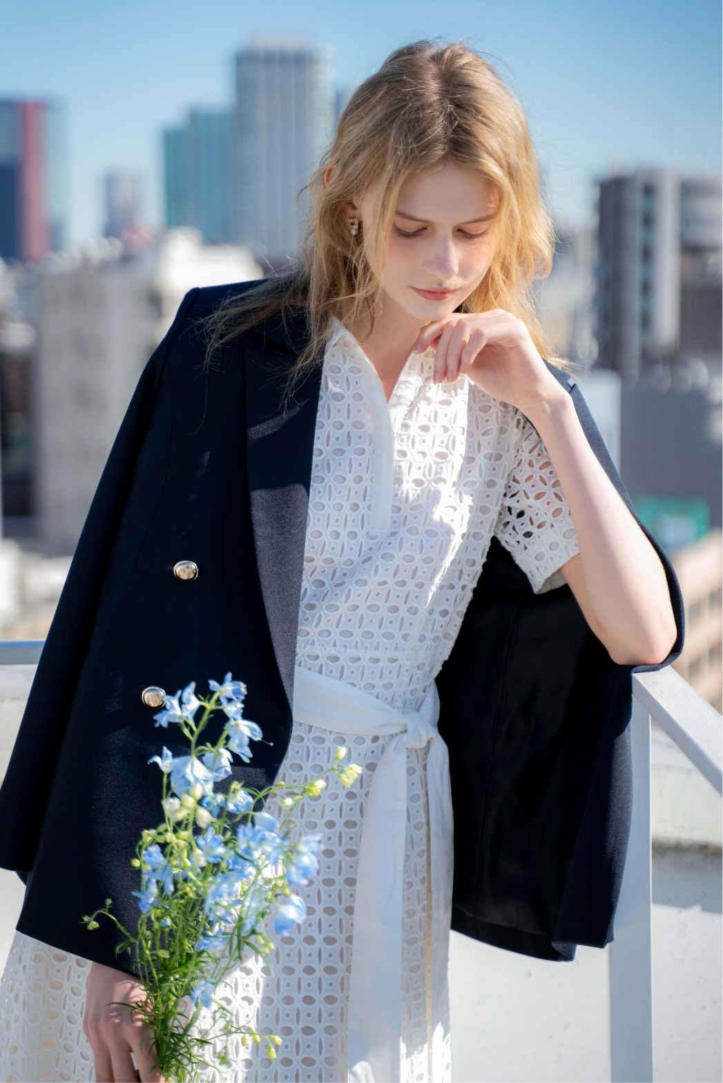 ダブルブレストジャケット・コットンレースシャツワンピース・スクエアビジューピアスを着用した女性