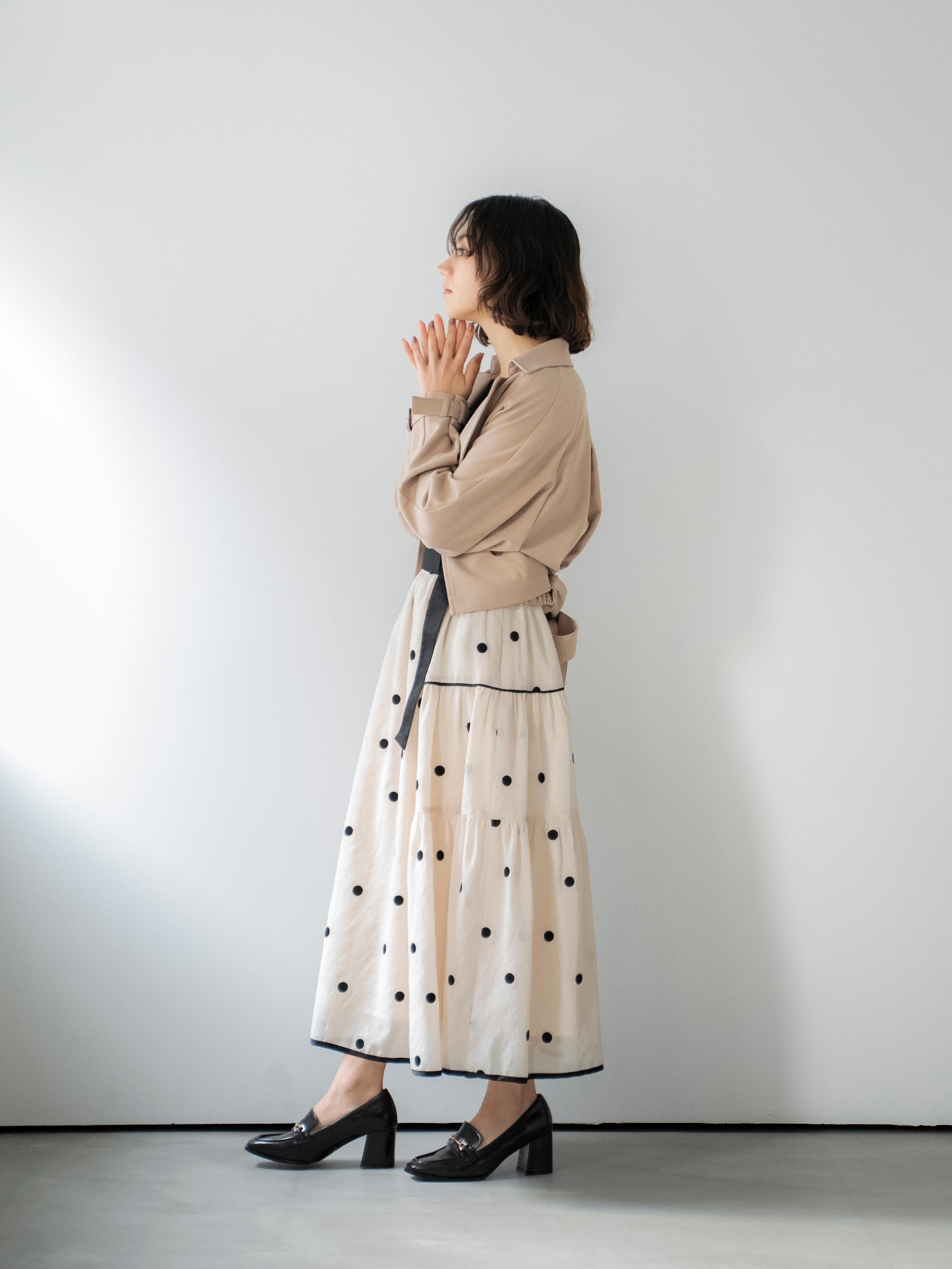 ラグランショートトレンチ・スカラネックデザインニット・ドット刺繍ティアードスカート・スクエアビットローファーを着用した女性の画像