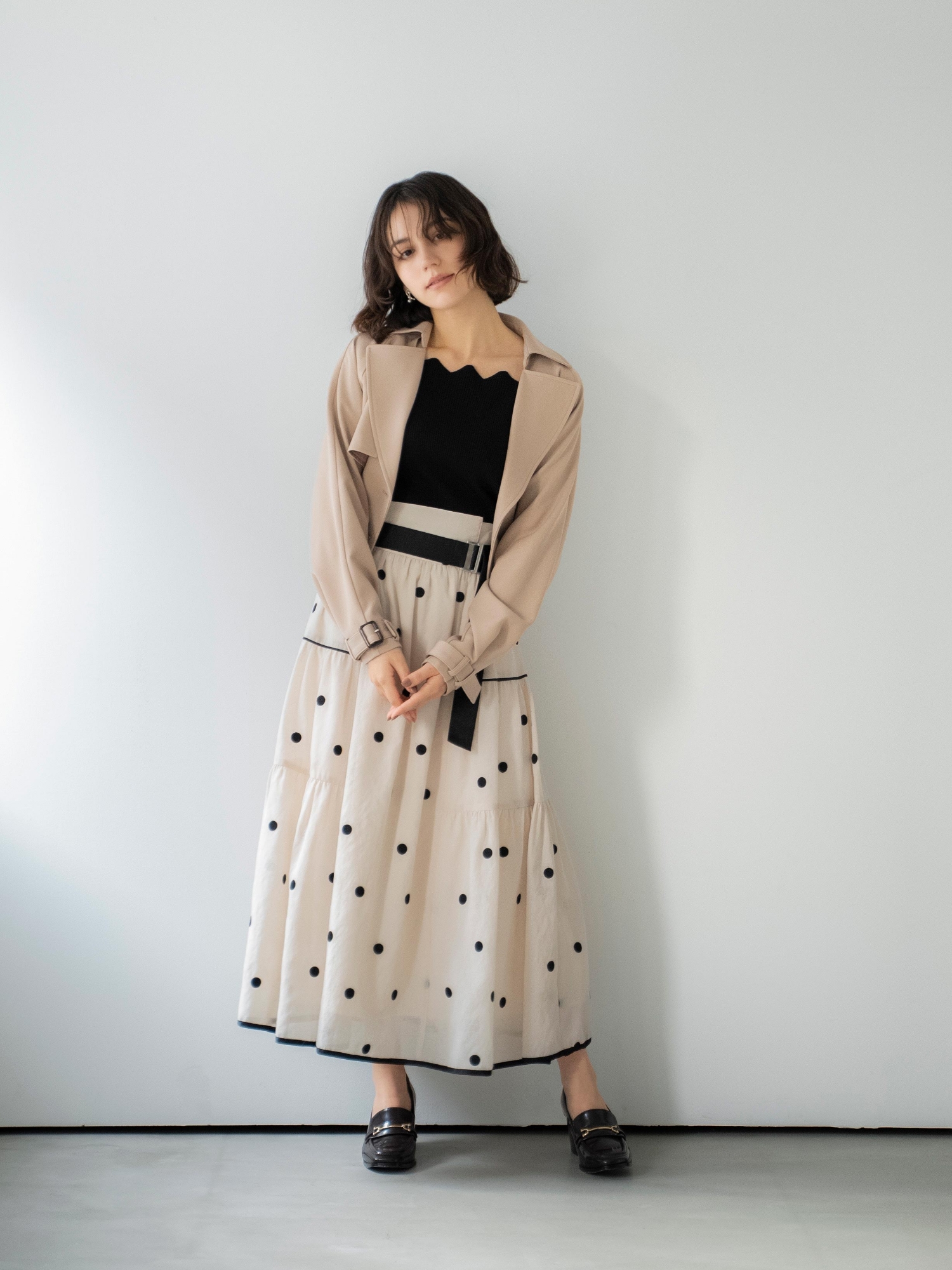 ラグランショートトレンチ・スカラネックデザインニット・ドット刺繍ティアードスカート・スクエアビットローファーを着用した女性の画像