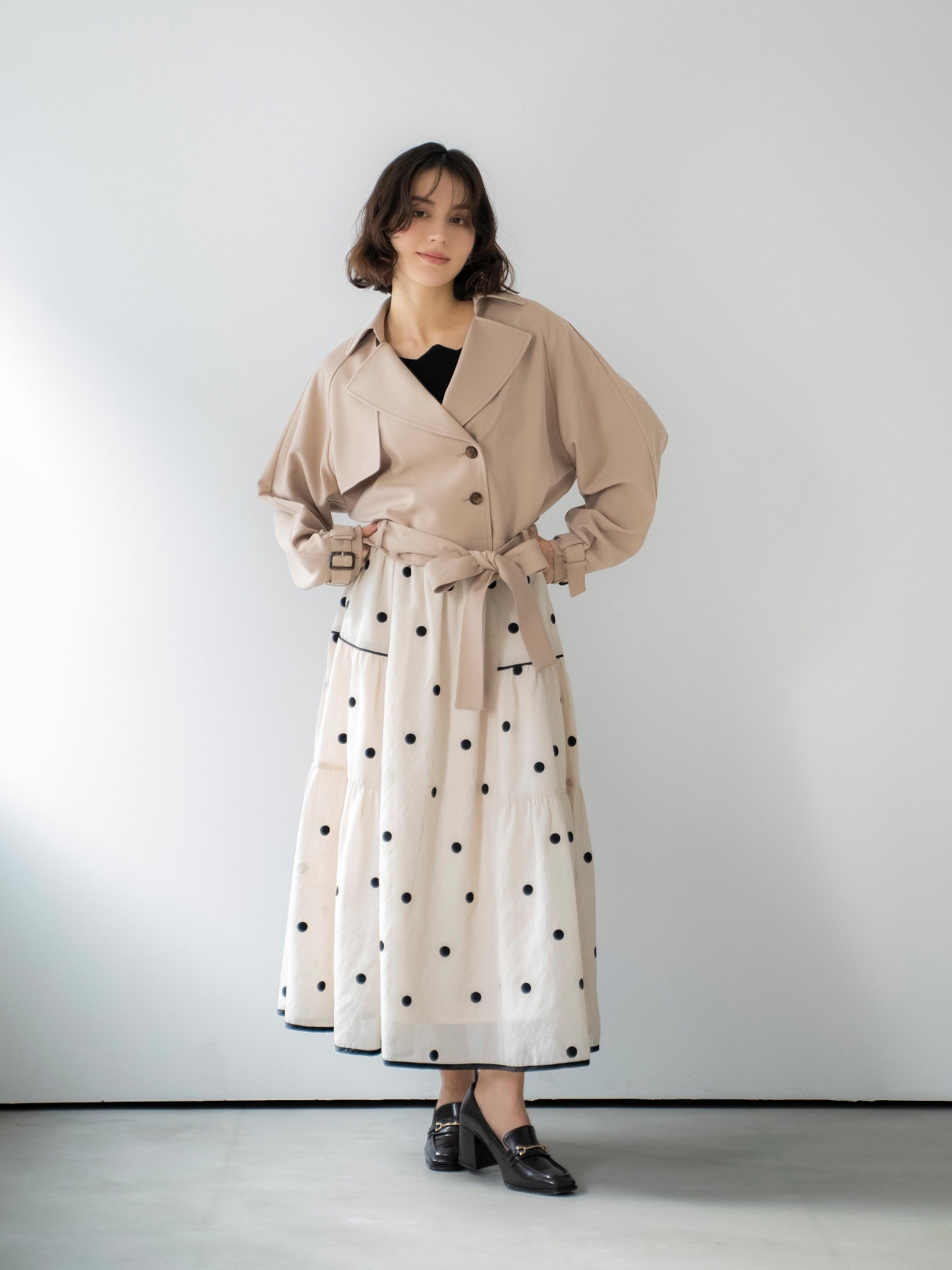 ラグランショートトレンチ・スカラネックデザインニット・ドット刺繍ティアードスカート・スクエアビットローファーを着用した女性の画像