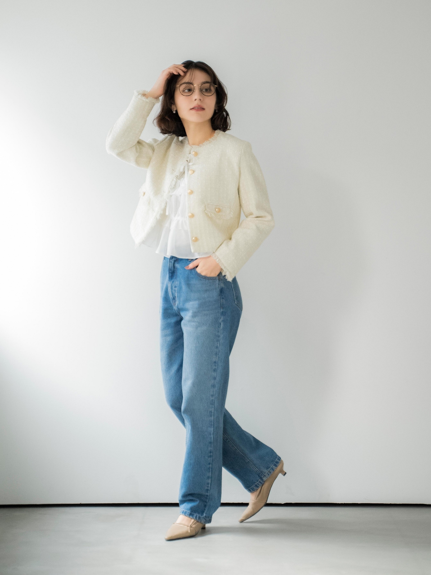 ツイードジャケット・シアーシャーリングブラウス・ストレートデニムパンツ・スクエアビジューピアス・サイドノットパンプスを着用した女性の画像