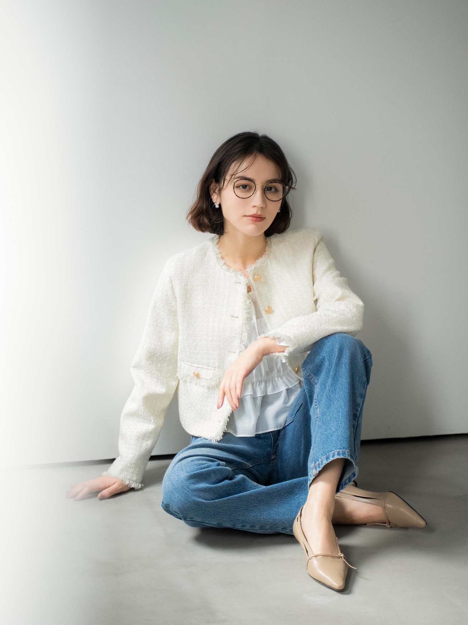 ツイードジャケット・シアーシャーリングブラウス・ストレートデニムパンツ・スクエアビジューピアス・サイドノットパンプスを着用した女性の画像