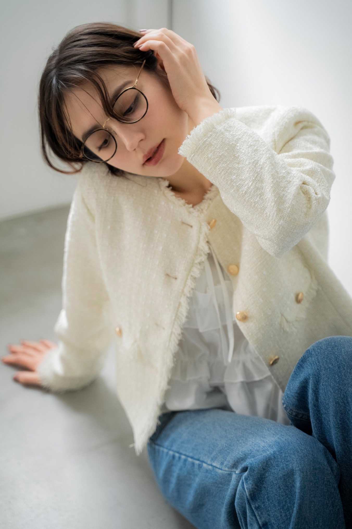 ツイードジャケット・シアーシャーリングブラウス・ストレートデニムパンツ・スクエアビジューピアスを着用した女性の画像